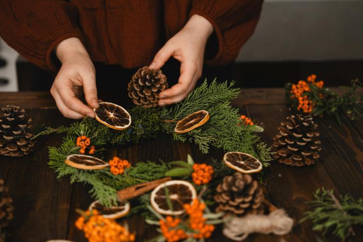 Una persona che fa da se una ghirlanda con pigne rami e fette di arancia secche