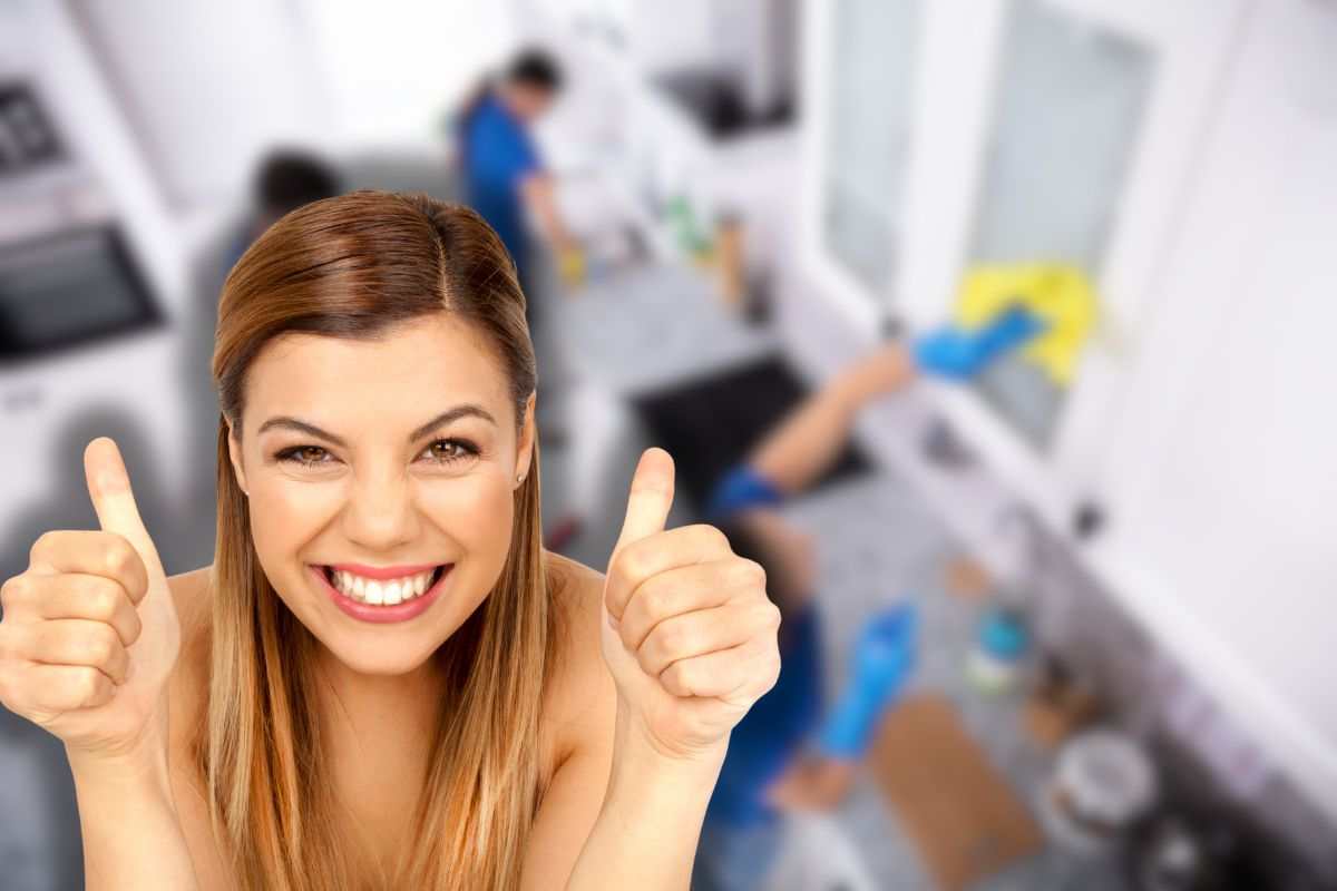 team di esperti che fa pulizie per casa sullo sfondo e donna sorridente che fa ok con le mani