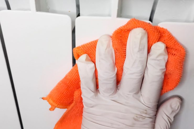 Una mano che indossa un guanto e usa una pezza per pulire un calorifero