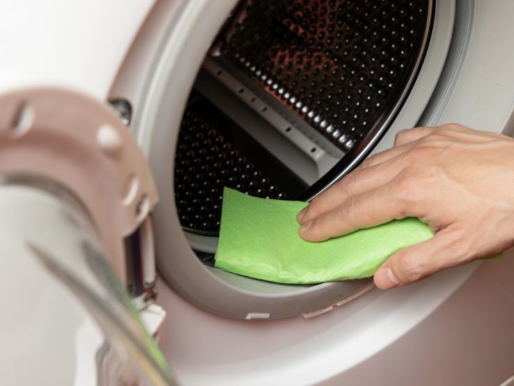 mano che mantiene una spugnetta verde e che pulisce l'interno della lavatrice