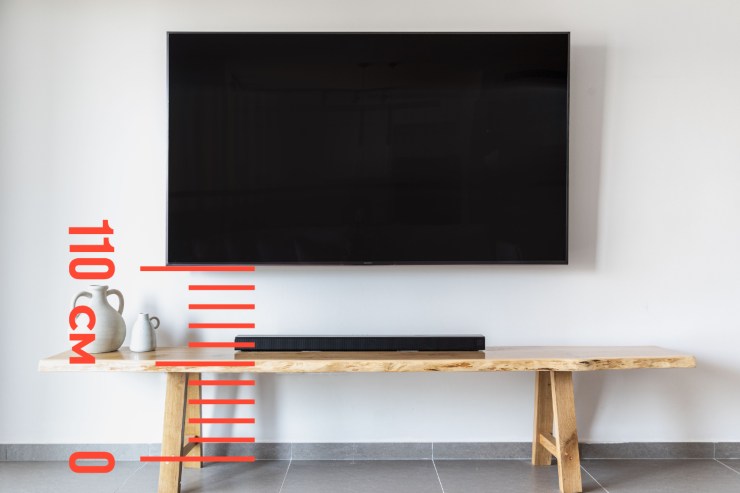 Una Tv attaccata al muro ed un metro che segna la distanza tra pavimento e TV di 110 cm