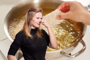 donna che si tappa il naso per la puzza di fritto che proviene da una pentola piena d'olio alle sue spalle