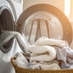Una lavatrice aperta dalla quale escono dei panni puliti e cadono in una cesta