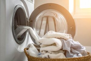 Una lavatrice aperta dalla quale escono dei panni puliti e cadono in una cesta