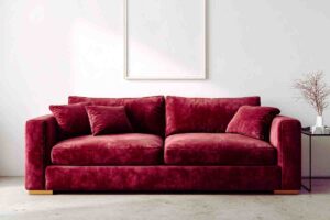 divano bordeaux in velluto in una stanza dai toni chiari, sotto un quadro vuoto