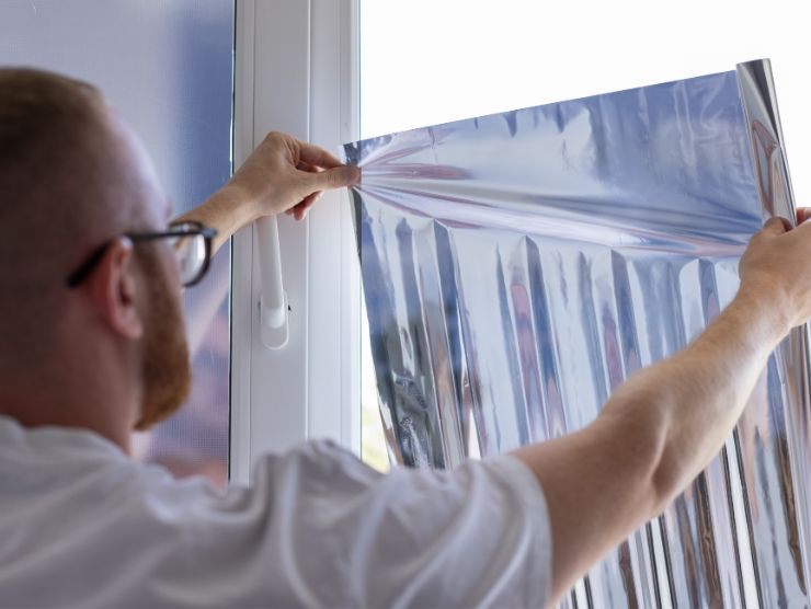 uomo che sta applicando una pellicola oscurante al vetro di una finestra