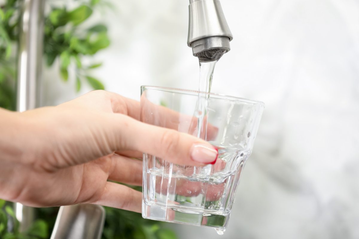 Una mano che riempie un bicchiere di acqua potabile dal rubinetto