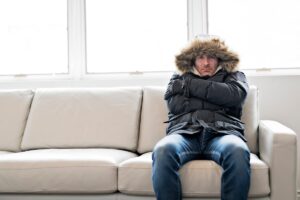 Un uomo che sente freddo con il giubbotto mentre sta seduto sul divano