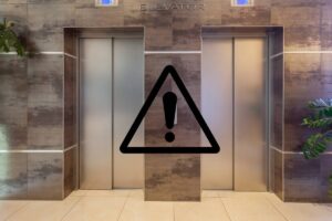 Una foto di due ascensori condominiali con in primo piano un segnale di pericolo