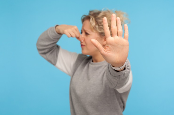 Una donna che con una mano si tappa il naso e con l'altra fa cenno di stop