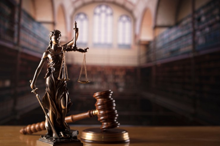 Un aula di tribunale con davanti un martello da giudice ed una statua di giustizia