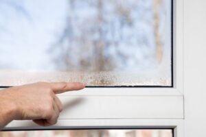 Una persona che indica l'umidità sul vetro della propria casa