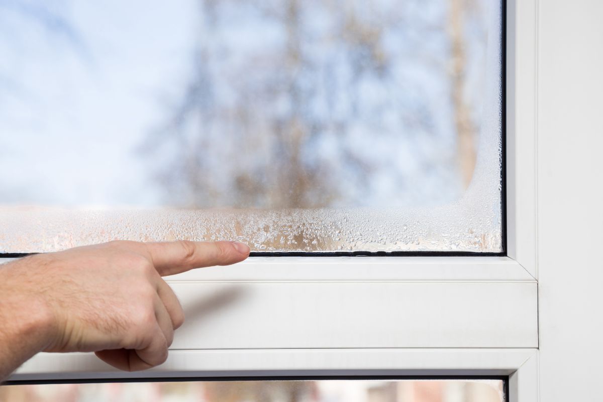 Una persona che indica l'umidità sul vetro della propria casa