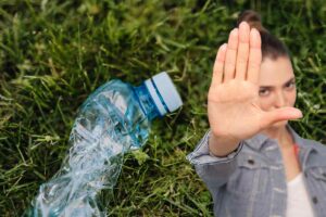 bottiglietta di plastica su prato e donna che fa segno stop con la mano