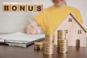 donna che firma fogli con casetta e soldi vicino e scritta bonus