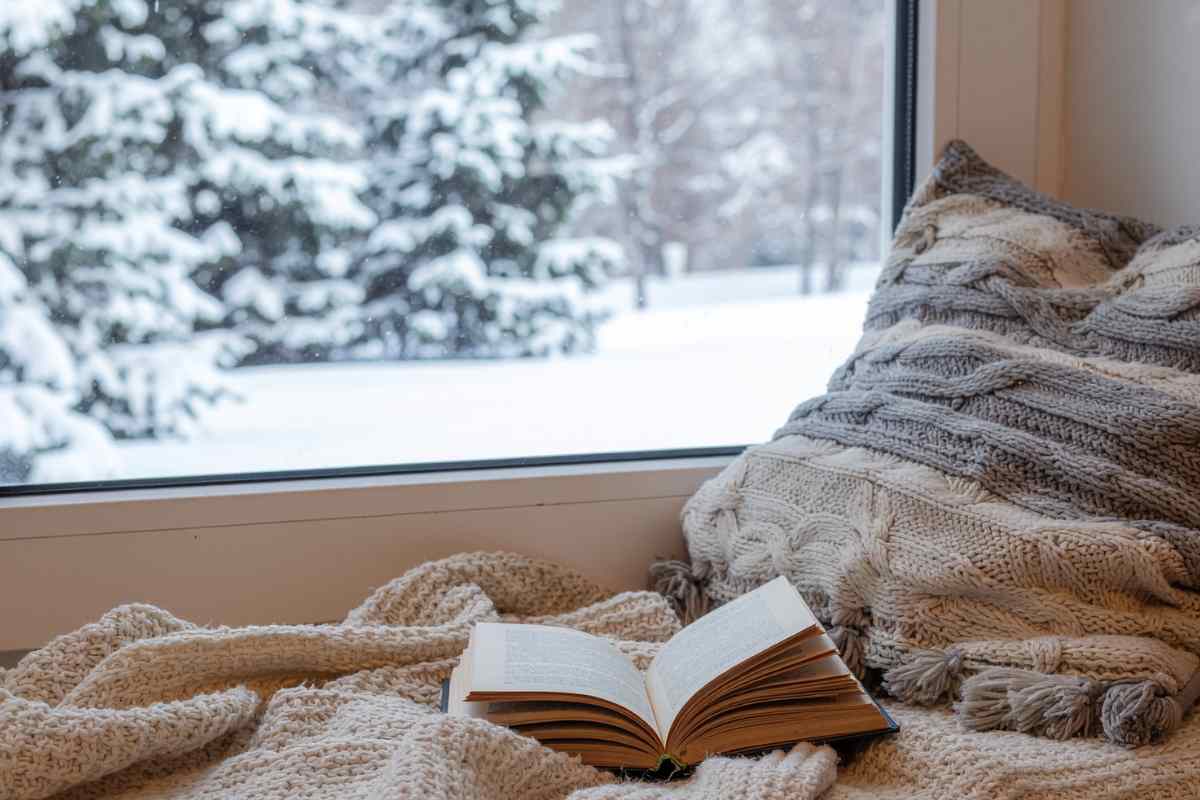 libro sul letto vicino ad una finestra con neve fuori