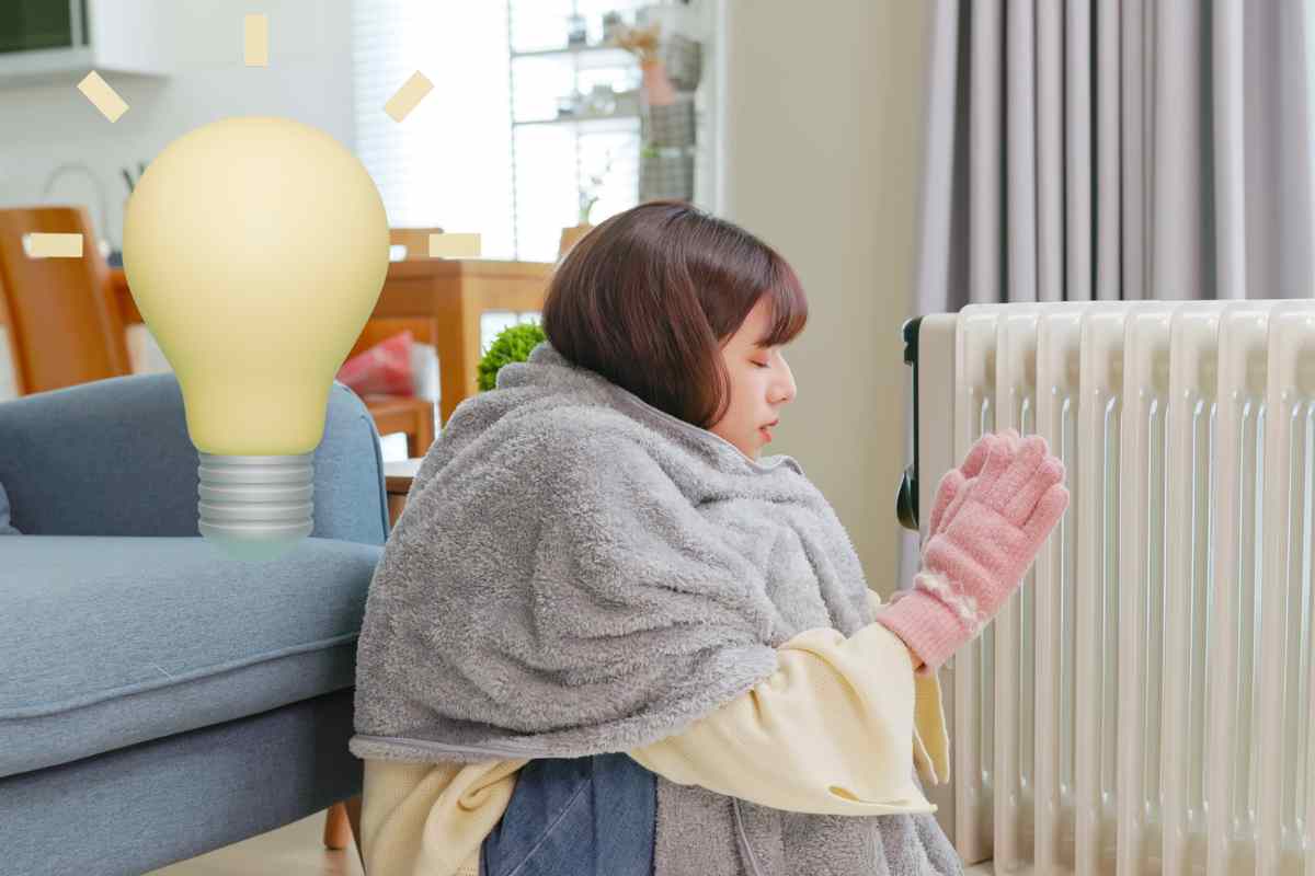donna davanti al termosifone che si scalda con coperta sulle spalle e lampadina