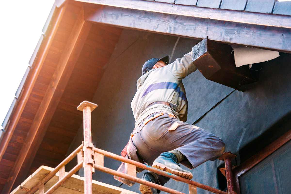uomo che dipinge parete esterna di una casa