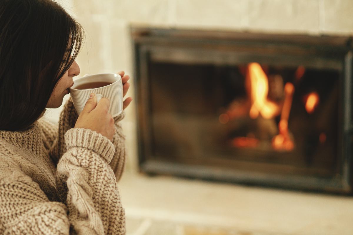 Una donna che beve una tisana calda davanti ad un camino in funzione