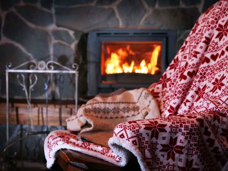 sfondo in cui si vede un camino acceso e in primo piano una poltrona con coperta 