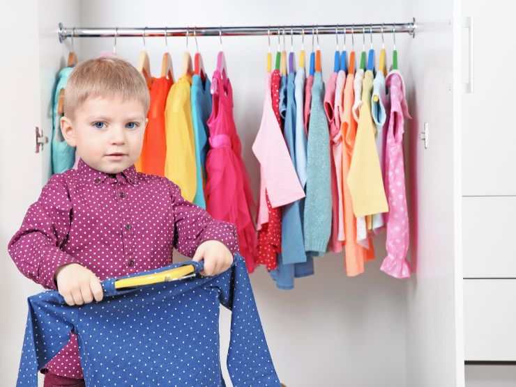 bambino con maglia in mano e armadio alle spalle