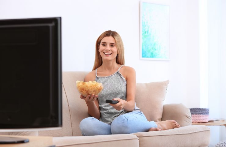 donna sorridente che guarda tv con patatine in mano