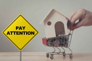 casa in un carrello della spesa e scritta attenzione in giallo