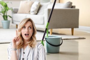 in primo piano una donna con un'idea e sfondo di un salotto in cui si vede secchio e mocio