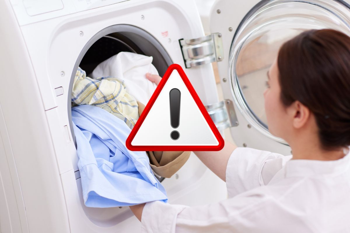donna carica lavatrice e segnale di pericolo in evidenza