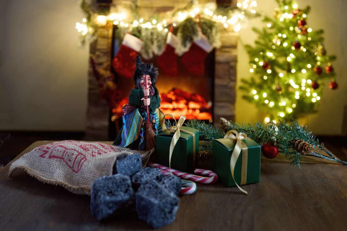 camino come sfondo e in primo piano una bambolina della befana con calze e regali