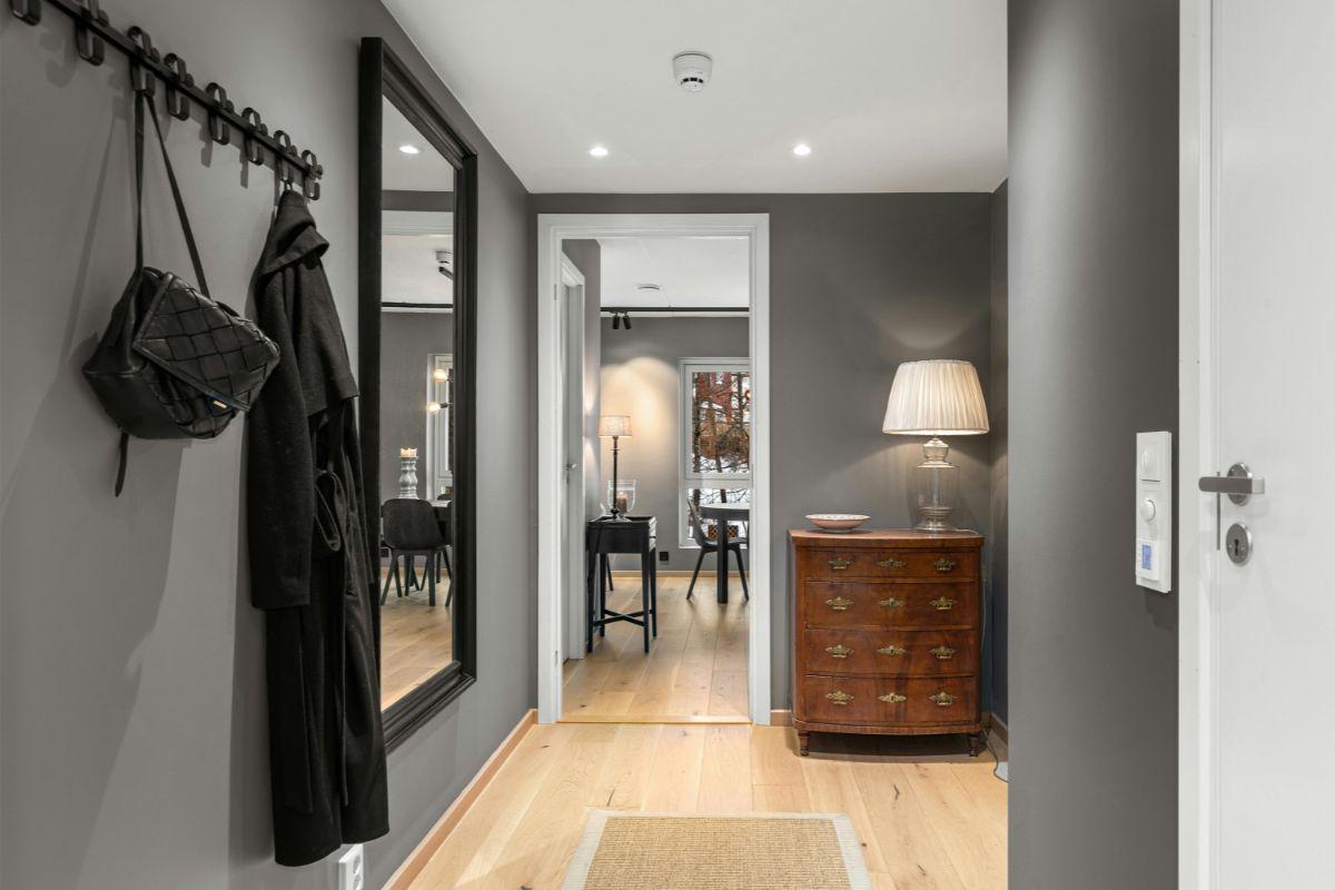 ingresso di un appartamento sui colori del grigio, in cui si vede uno specchio e un cappotto appeso