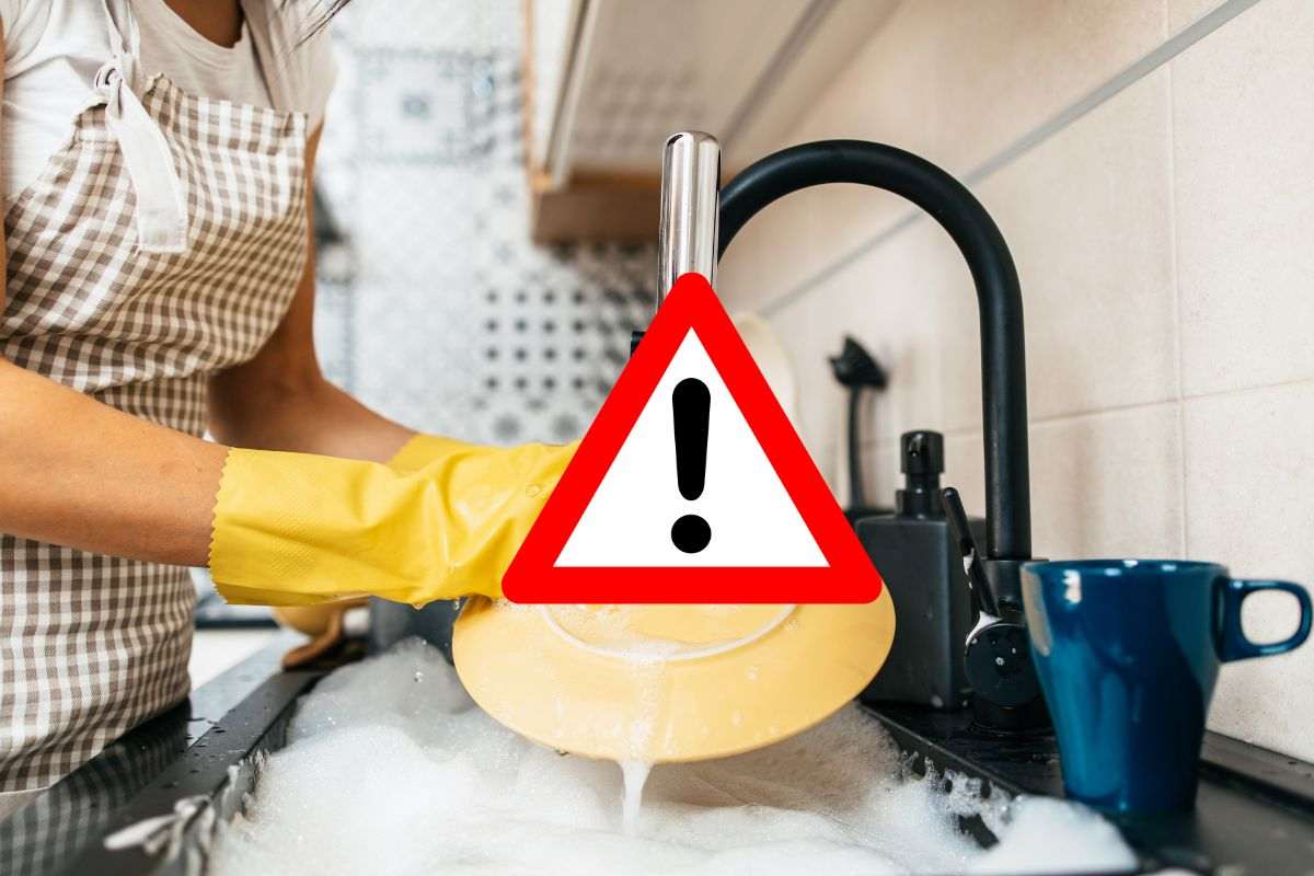 donna lava i piatti a mano e segnale di pericolo in evidenza