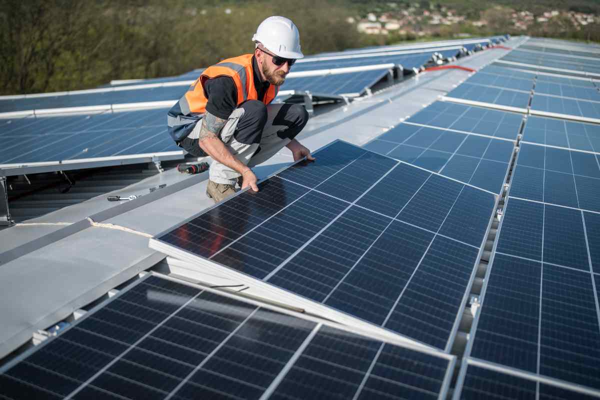 pannelli fotovoltaici e uomo che li installa su di un tetto
