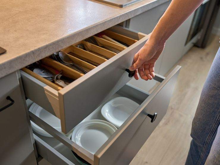 mano che apre cassetto della cucina in cui si cedono piatti e posate