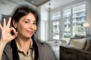 soggiorno di casa con piante sullo sfondo e donna sorridente che fa ok con le mani in primo piano