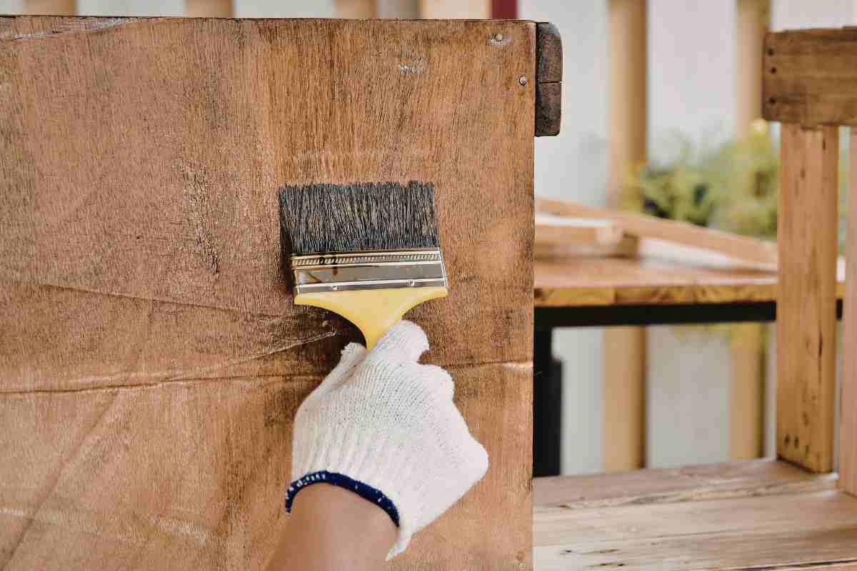 mano che passa pennello su legno con guanto 