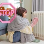 Una donna che sente freddo in casa e indossa coperta guanti e sta vicino al termosifone