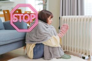 Una donna che sente freddo in casa e indossa coperta guanti e sta vicino al termosifone