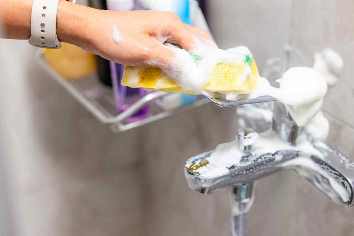 mano che pulisce con spugna un rubinetto