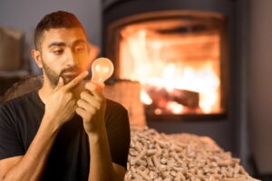 uomo con alle spalle stufa a pellet e lampadina in mano con idea