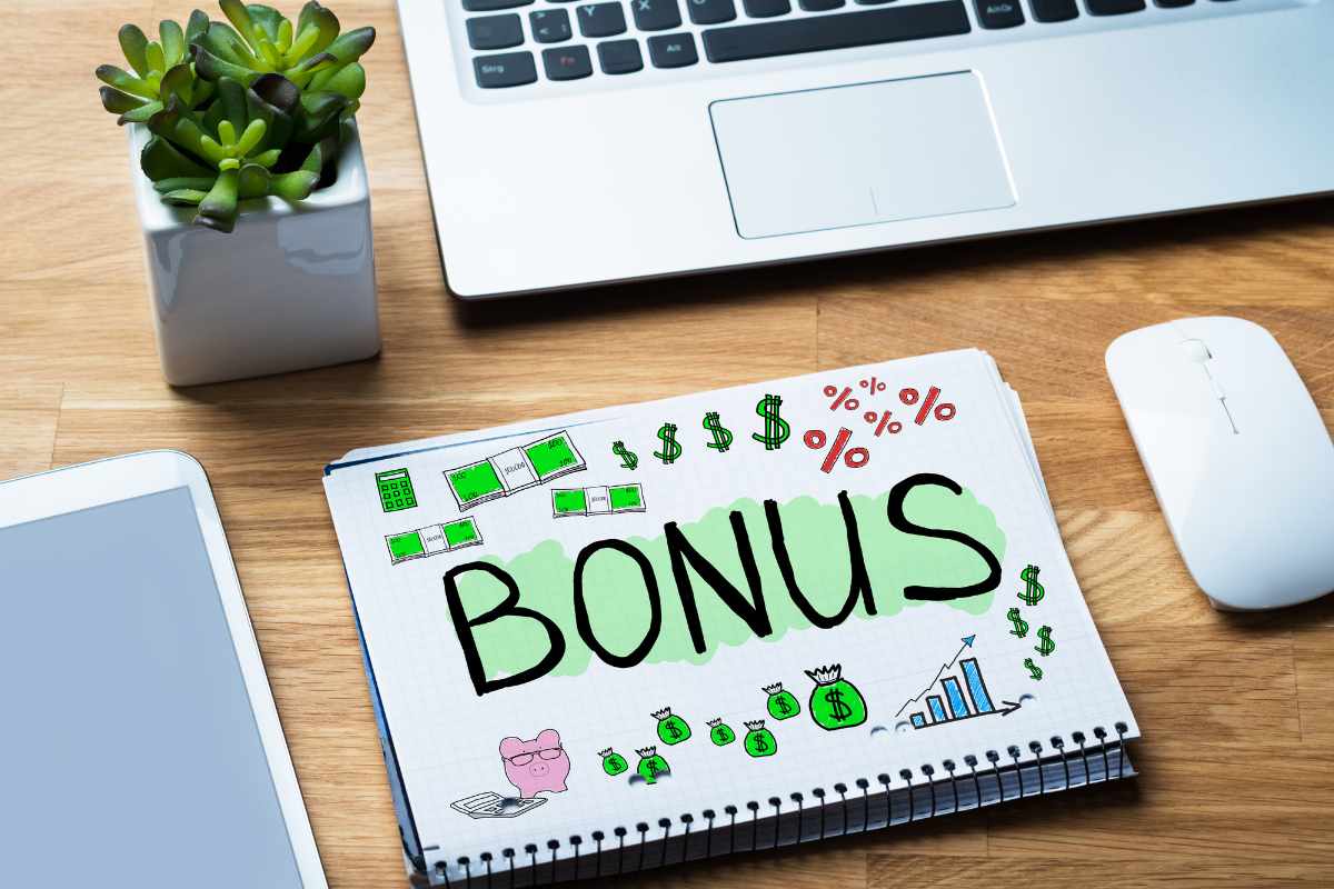 Una scrivania con sopra un computer un mouse e un quaderno con sopra disegnato una scritta "Bonus"