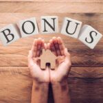 Le mani di una persona che tengono la miniature di una casa in legno, con sopra una scritta bonus