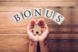 Le mani di una persona che tengono la miniature di una casa in legno, con sopra una scritta bonus