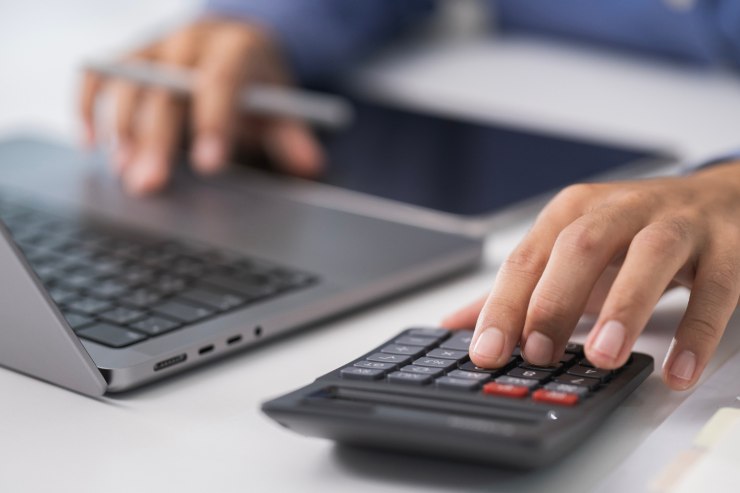 Un uomo al computer che fa calcoli con la calcolatrice