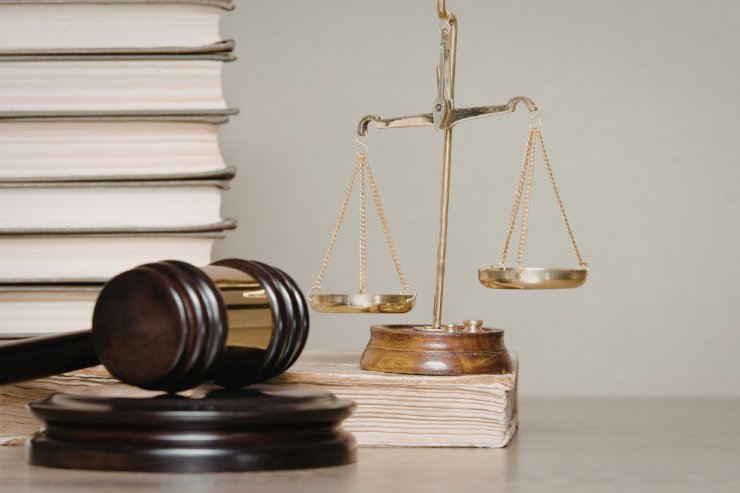 Un tavolo con sopra libri, martello da giudice ed una bilancia di giustizia