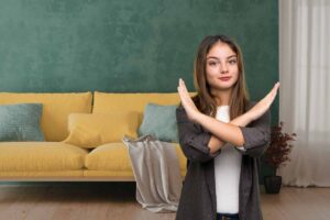 Un divano contro il muro ed una donna in primo piano che fa una croce con le mani