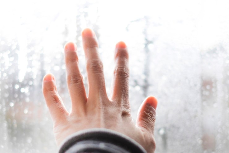 Una mano che tocca un vetro bagnato per via dell'umidità