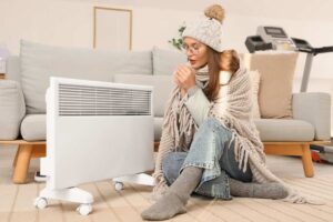 Una donna che sente freddo in casa e si mette vicino ad una stufa ed indossa cappuccio e sciarpa