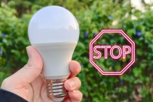 Una mano che tiene una lampadina al LED ed un segnale di Stop sulla destra