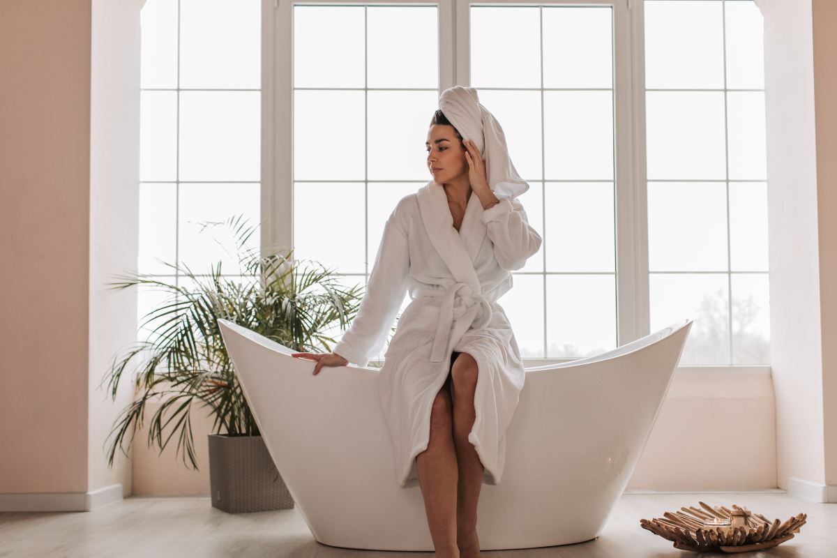 Una donna in accappatoio seduta sul bordo di una vasca bianca